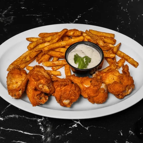 Crispy fried chicken wings and golden french fries with a side of creamy dip on a white plate.