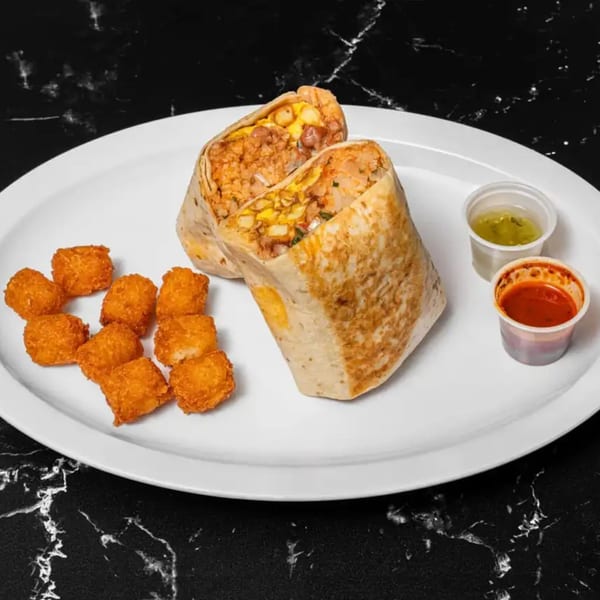 Two halves of a large burrito with tater tots and two dipping sauces on a white plate.
