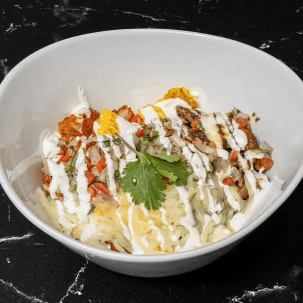 A white bowl filled with Mexican food, topped with pico de gallo, sour cream, and cilantro.