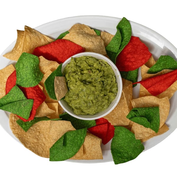 A white plate holds a bowl of guacamole surrounded by red, green, and yellow tortilla chips.
