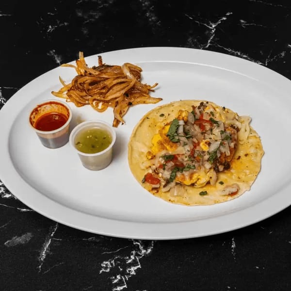 A Tacos El Primo taco with onions, salsa, and green sauce on a white plate.