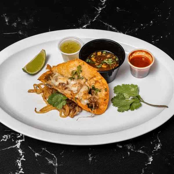 A Tacos El Primo birria taco with melted cheese, onions, cilantro, lime, and dipping sauces.