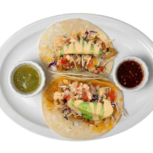 Two fish tacos with cabbage, pico de gallo, avocado, and sauce, served with green and red salsas.